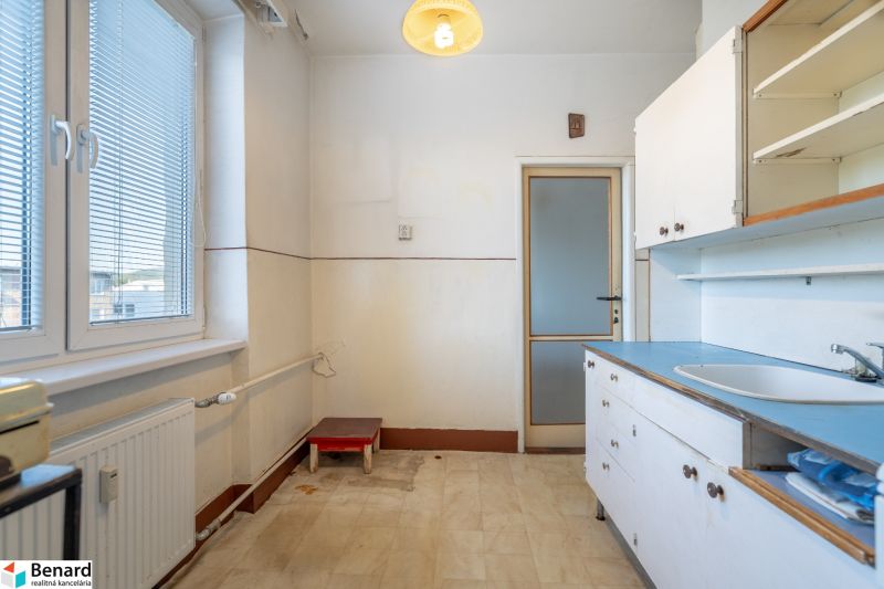 A kitchen in a 2-room apartment with white cabinets and a large window.