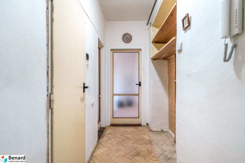 A hallway in a 2-room apartment with shelves and a floor with a wooden decor.