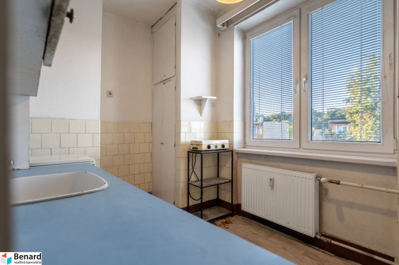 A kitchen with white tiles, a blue countertop in a 2-room apartment, a large window, simple interior.