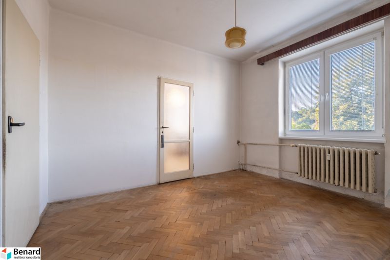 A room in a 2-room apartment with a wooden decor floor and a radiator.