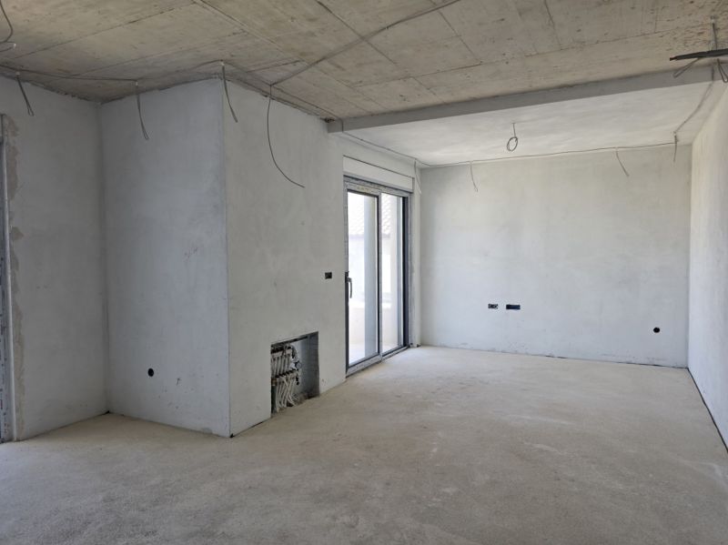 Interior of an empty room with a concrete ceiling and a large window in a 3-room apartment.