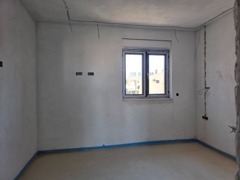 Empty room in a 3-room apartment with a large window and white walls.