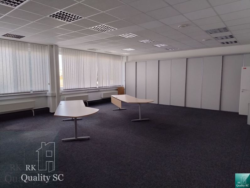 Offices with carpeted floors, white vertical blinds, and contrasting desks.