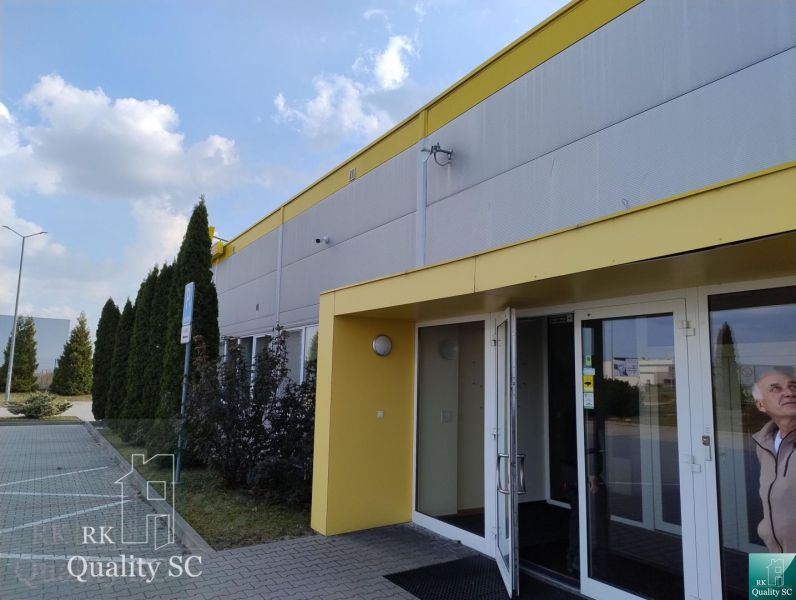 Exterior of a building in Senec with a parking lot and a yellow entrance to the offices.