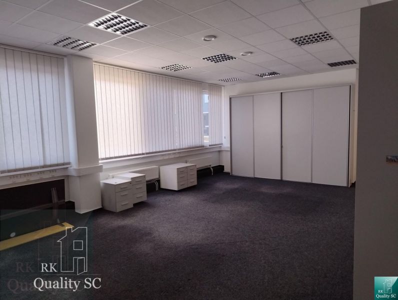 Spacious offices with white furniture and dark carpet, large windows with blinds.
