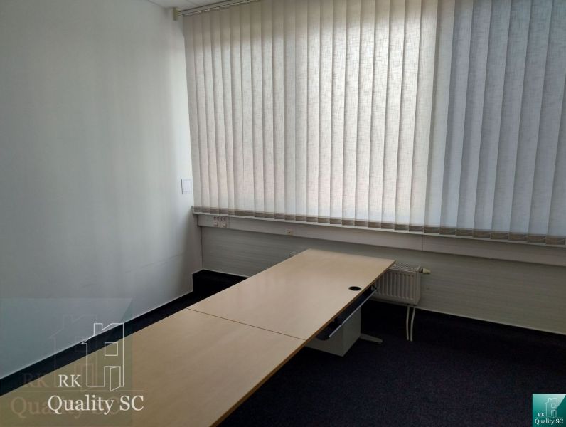 A bright office with a long table, blinds, and carpet.