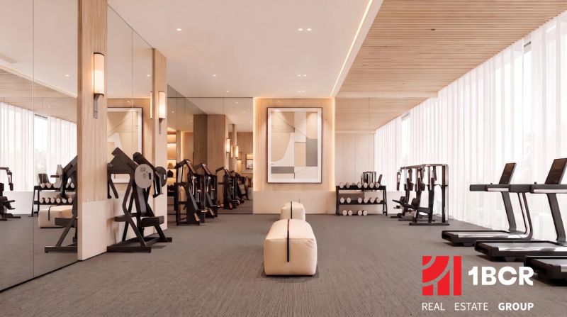 Fitness space with wood-patterned flooring, mirrors, and exercise equipment in an apartment development.