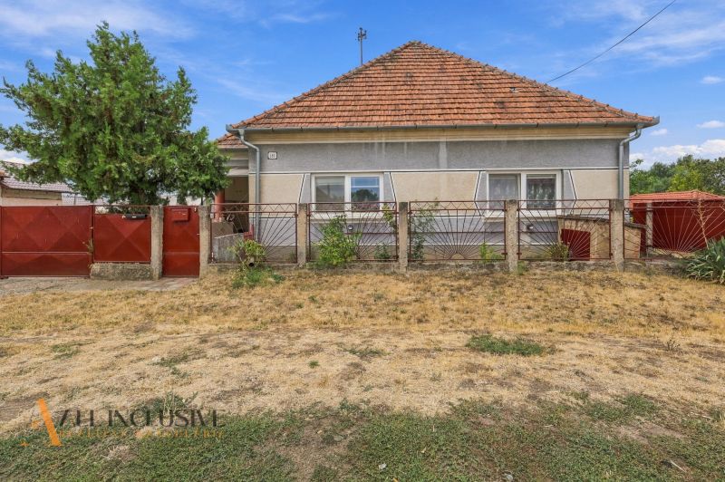 A family house in Bátorove Kosihy with a red roof and fence. Dried lawn.