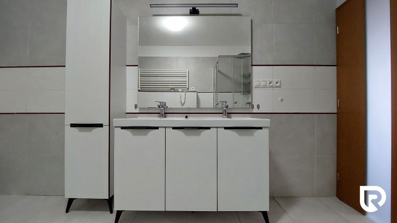 A bathroom with a double sink in a two-room apartment, white cabinet, large mirror.