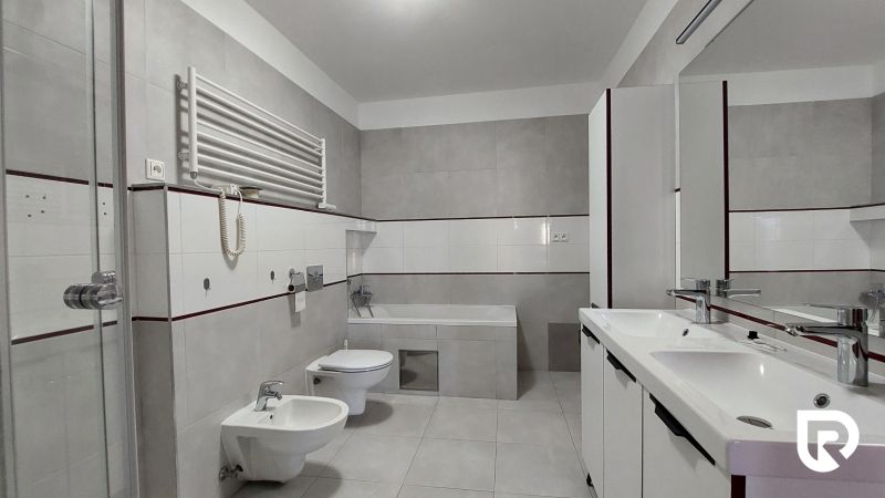 A bathroom with a bathtub, shower, and double sink in a 2-room apartment.