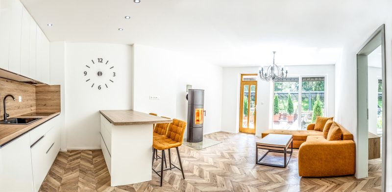 Bright holiday apartment with a kitchen, orange sofa, and wood-patterned flooring.