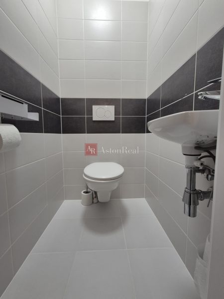 A minimalist toilet in a 3-room apartment with white and dark tiles.
