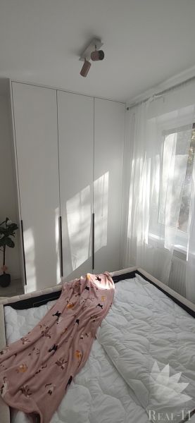A bright bedroom with a built-in wardrobe, curtains, and a bed in a three-room apartment.