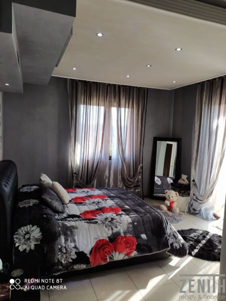 A bedroom in a villa with windows, a mirror, and a bed with a floral pattern.