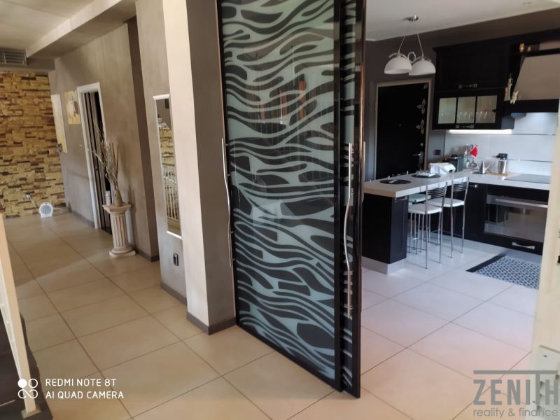 Interior of a villa with glass doors and a kitchen, floor with wood decor.