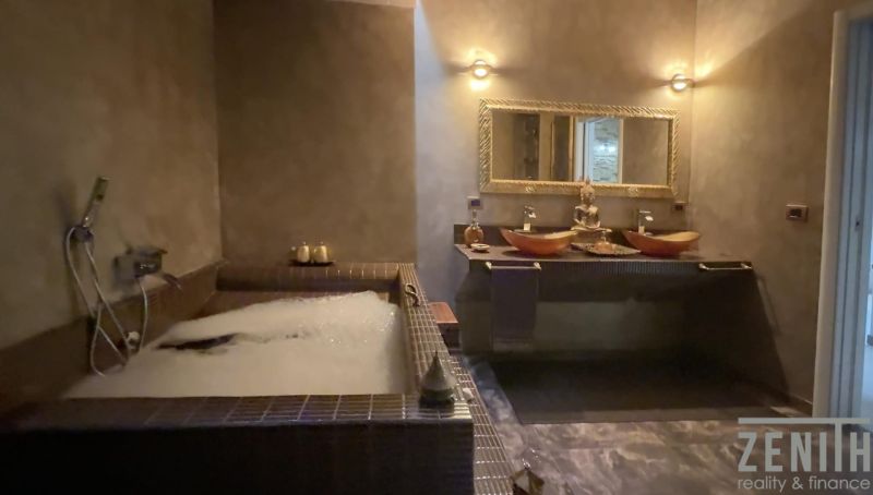 A bathroom in a villa with a hot tub, mirror, and decorative figurine on the sink counter.