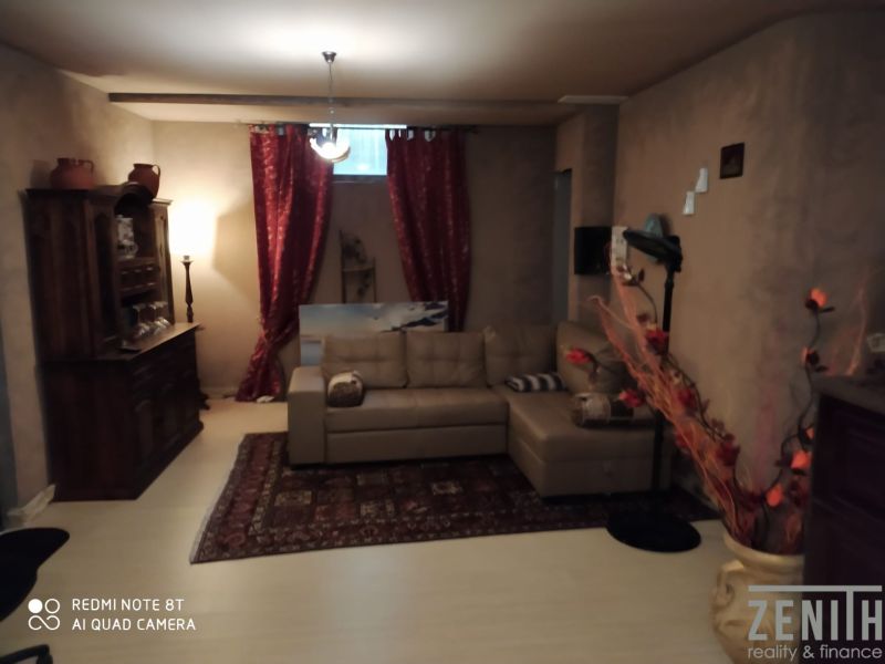 Living room in a villa with a sofa, curtains, decorations, and a wooden-patterned floor.