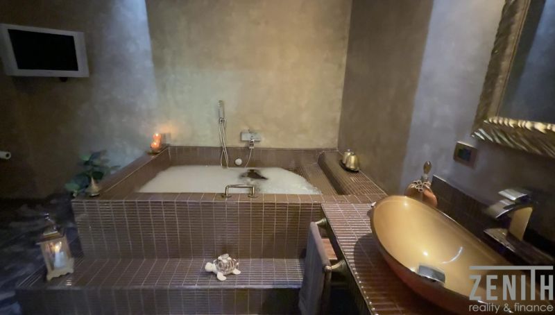 A luxurious bathroom in a villa with a bathtub surrounded by ceramic tiles and accessories.