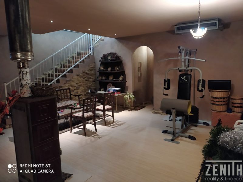 Interior of a villa with a fitness machine, a sofa set, and a wooden decor floor.