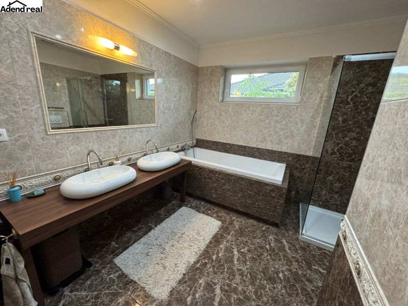 A bathroom in a family house with a shower, a bathtub, a double sink, and marble walls.