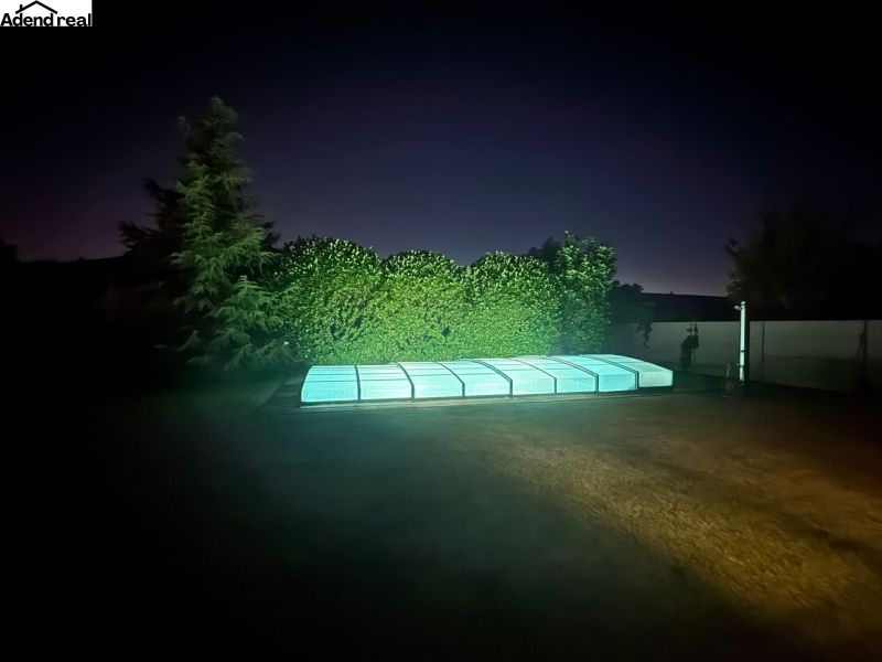 The garden of a family house on Slnečnicová Street in Miloslavov with a lit-up pool at night.