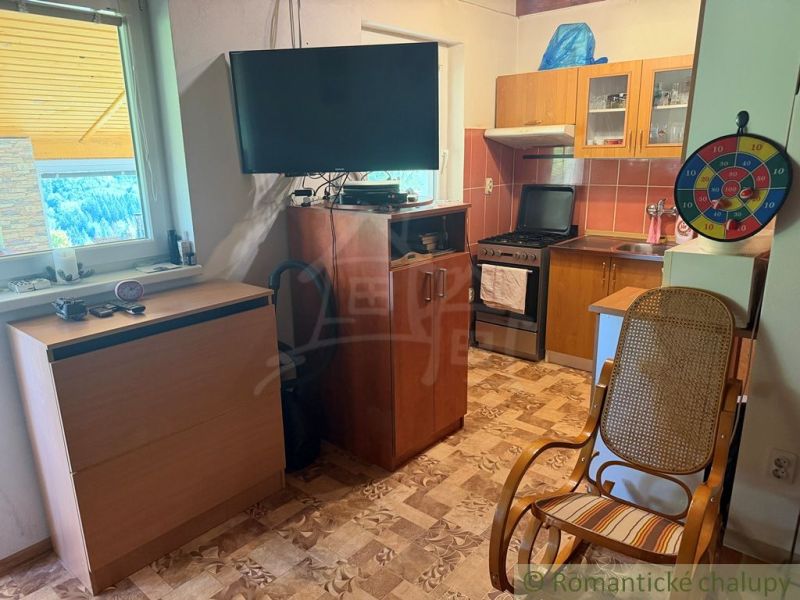 Interior of a cottage with a television, kitchen unit, stove, and comfortable armchair.
