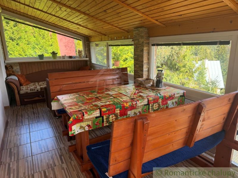 A wooden interior of a cabin with seating, a table, and a view of nature.