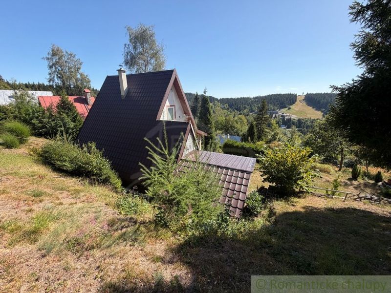 A cottage in Látky surrounded by greenery, with a view of forests and mountains.