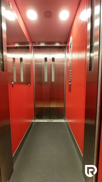 The interior of a red elevator in a three-room apartment with mirrored elements on the walls.