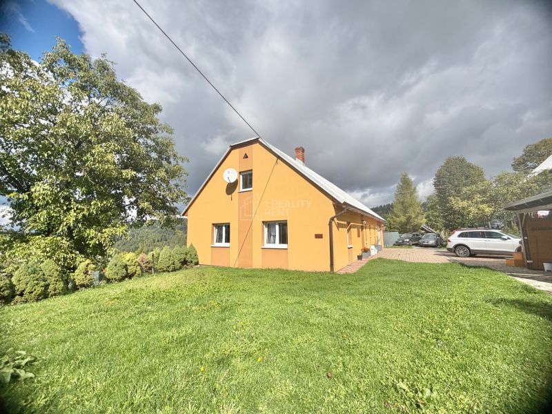 A family house in Oščadnica on Košariská Street with a grassy plot and parked cars.