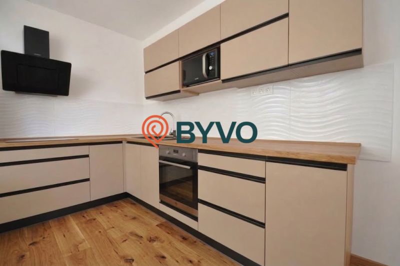 A kitchen in a 2-room apartment with a wooden decor floor and light cabinets.