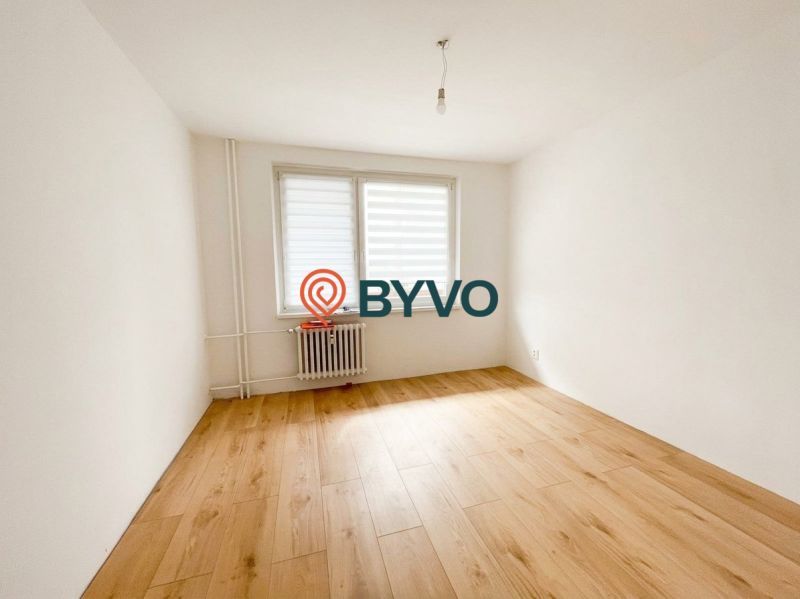 A room in a 2-room apartment with a wooden decor floor and a large window.