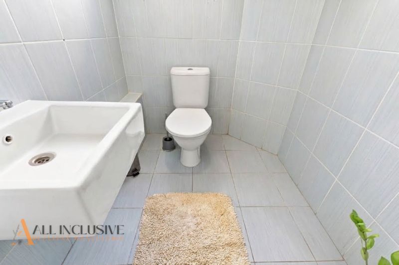 Bathroom in a family house with a sink, toilet, and beige rug.