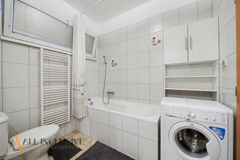 A bathroom in a studio apartment with a sink, washing machine, bathtub, and radiator.