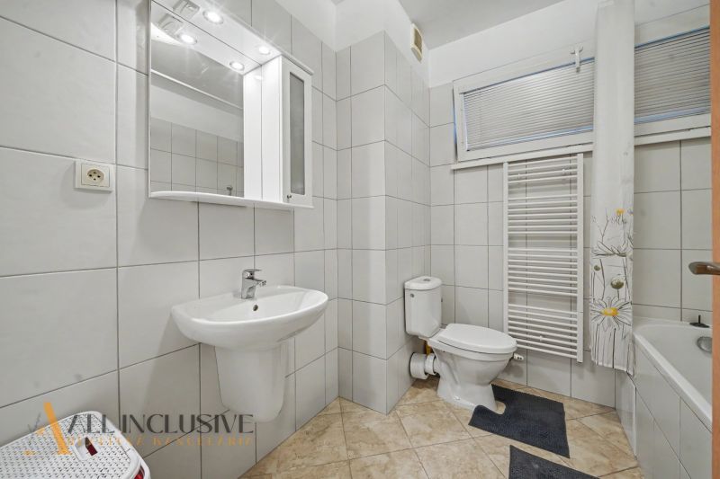 A bathroom in a studio apartment with a sink, bathtub, and ladder radiator.