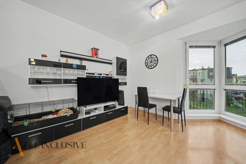 Living room in a studio apartment with furniture, a television, and a wooden decor floor.