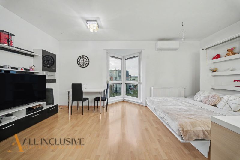 Living room with wood-patterned flooring, a bed, and a table in a studio apartment.