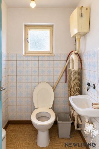 A bathroom in a family house with a toilet and a sink, floor with a wooden decor.