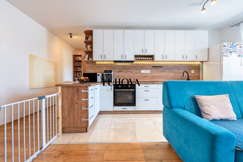 A kitchen in a 3-room apartment with white cabinets, a blue sofa, and a floor with a wooden decor.