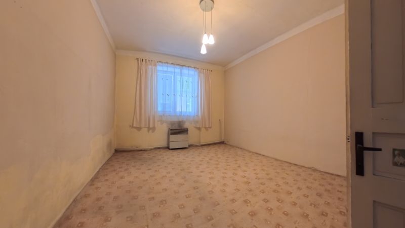 An empty room in a family house with a carpet, a heater, and curtains on the window.