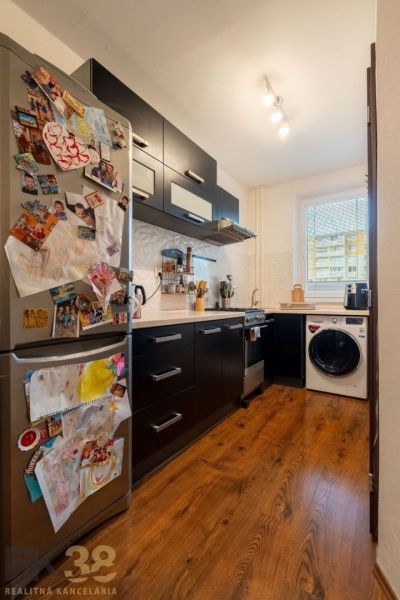 A kitchen in a 3-room apartment with a wooden decor floor and black furniture.