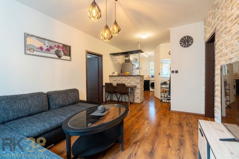 Living room in a 3-room apartment with a wooden decor floor, a sofa, and a kitchenette.