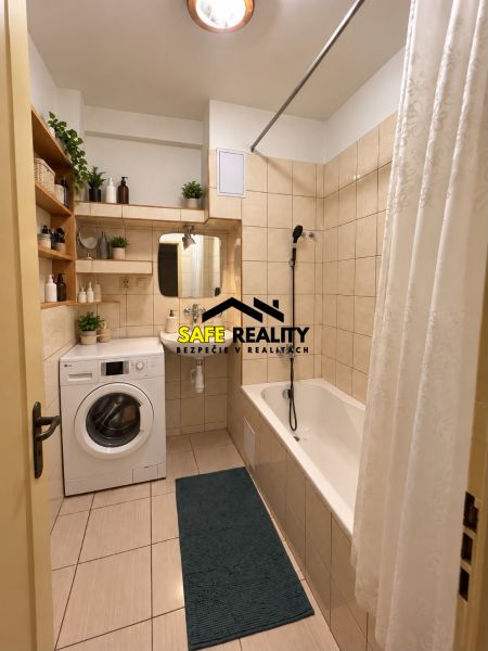 A bathroom in a one-room apartment with a bathtub, washing machine, and shelves for decorations.