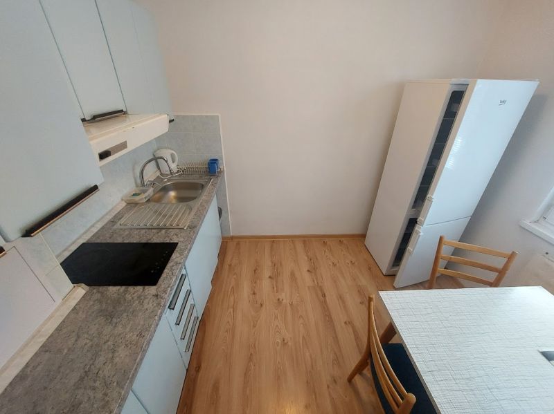 A kitchen in a studio apartment with a wood-patterned floor and white cabinets.