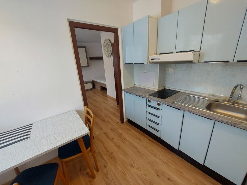 A kitchen with blue cabinets, a wooden decor floor, and a dining table in a studio apartment.