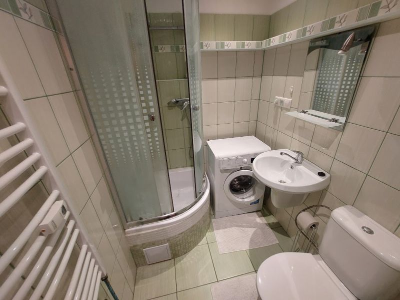 Bathroom in a one-room apartment with a washing machine, shower, sink, and toilet.