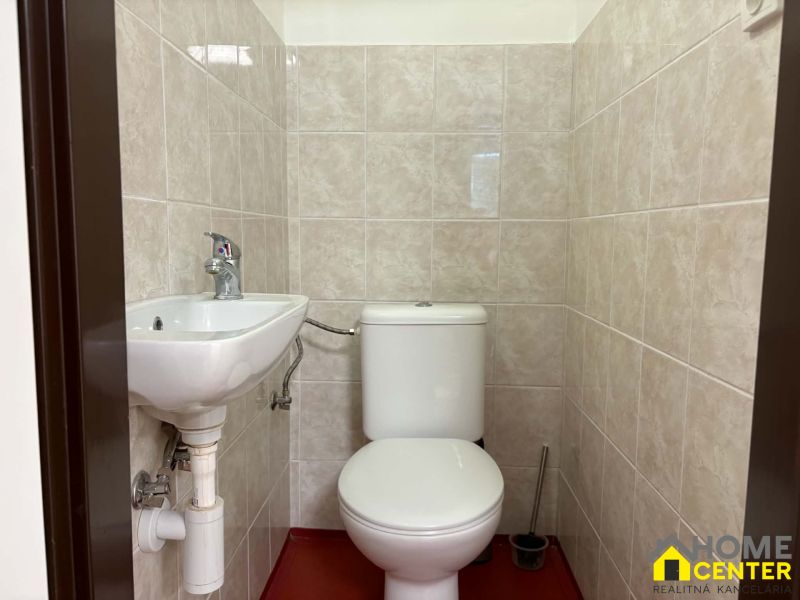 Toilet and sink in offices with tiled walls.