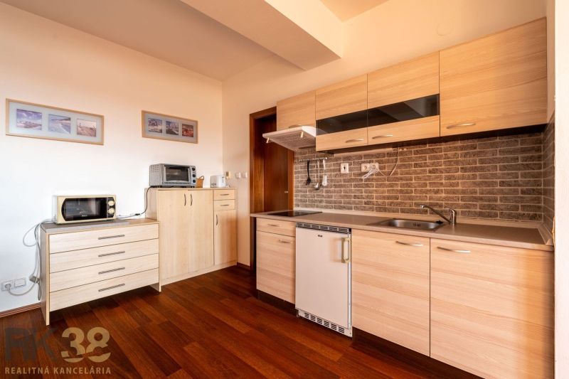 The kitchen of a 2-room apartment with a wooden decor floor and light furniture.