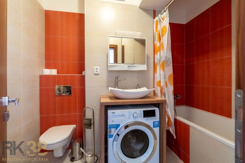A bathroom in a 2-room apartment with a washing machine, a bathtub, and orange tiles.
