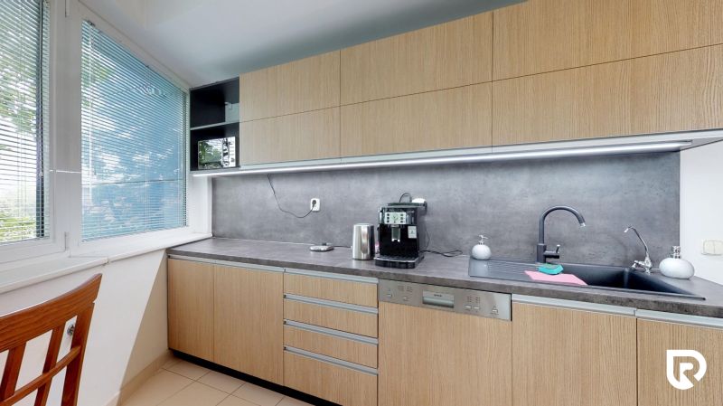 Office kitchen area with wooden cabinets and a large window with blinds.
